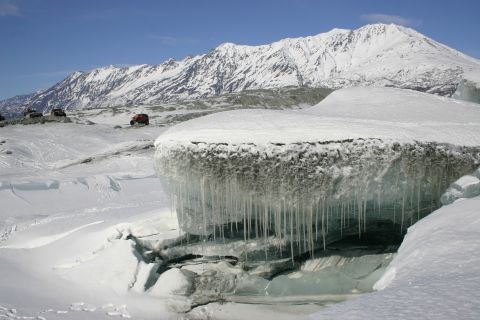2003 Jeep TJ - Two red off-road vehicles traverse a snowy terrain with a glacier and mountains under a clear blue sky.
