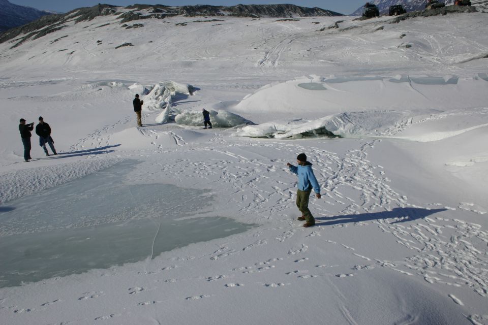Four-wheel drive vehicles parked on a snowy slope with people nearby