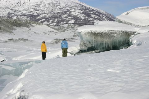 2003 Jeep TJ - Two individuals observe the icy landscape of a glacier under a clear blue sky, with a snow-covered mountain in the distance.