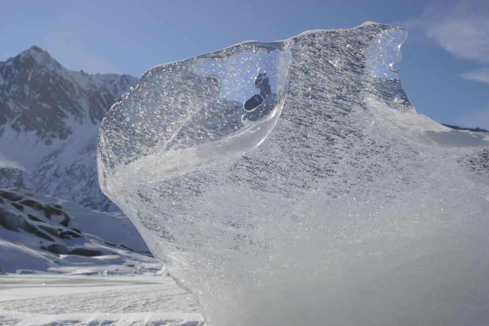 Ice formation with a hole in it, with snowy mountains and a blue sky in the background