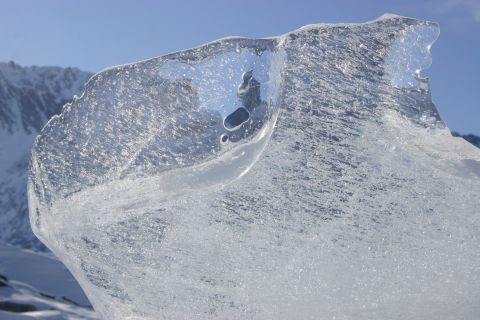 2003 Jeep TJ - A detailed view of a glacial ice chunk, its internal structure and clarity under a clear sky with distant mountain peaks.