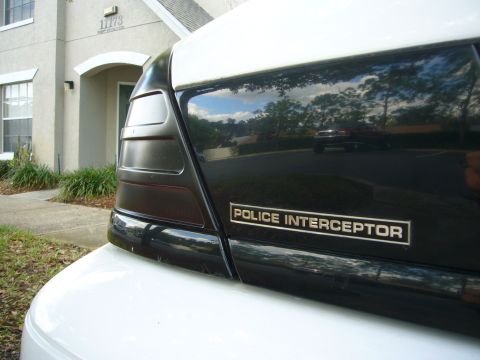2000 Ford Crown Victoria - Close-up of the rear of a white Ford Crown Victoria showing the gold-lettered "POLICE INTERCEPTOR" badge on the black trunk panel and the s…
