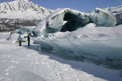 2003 Jeep TJ - Two individuals observe massive ice formations in a snowy landscape, with a mountain range visible in the distance.