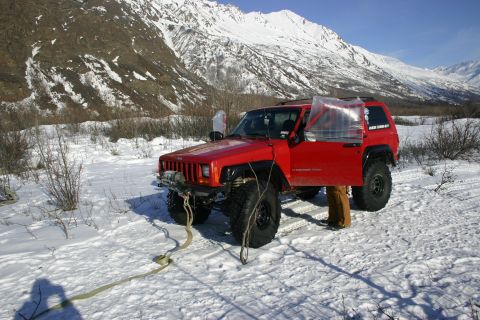 2003 Jeep TJ - A red Jeep Cherokee XJ is parked in a snowy landscape, with its driver's door open and a winch attached to the front bumper.