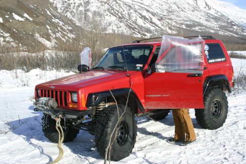 2003 Jeep TJ - A red Jeep Cherokee with its driver's door open and a winch mounted on the front bumper sits in a snowy landscape.