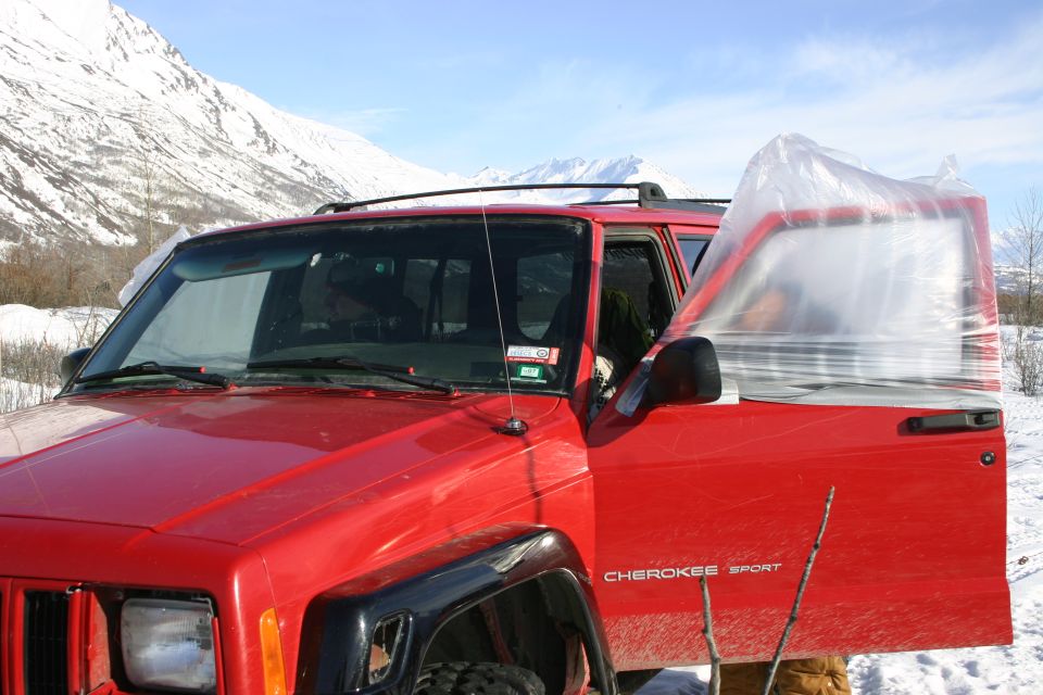 Red Jeep Cherokee Sport with driver's door open and covered in plastic