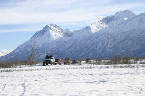 2003 Jeep TJ - Off-road vehicles traverse a snowy terrain with snow-capped mountains under a blue sky.