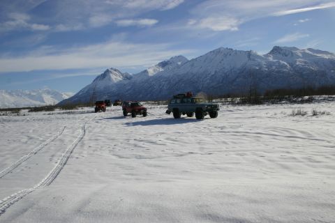 2003 Jeep TJ - A group of SUVs traverse a snow-covered plain under a partly cloudy sky, with snow-capped mountains dominating the horizon.