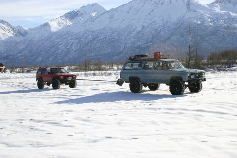 2003 Jeep TJ - Two modified SUVs traverse a snow-covered plain under a bright sky, with snow-capped mountains in the background.