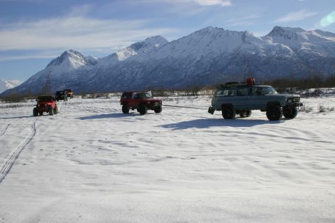 2003 Jeep TJ - Multiple off-road vehicles navigate a snow-covered terrain, with one SUV towing a Jeep towards snow-capped mountains.