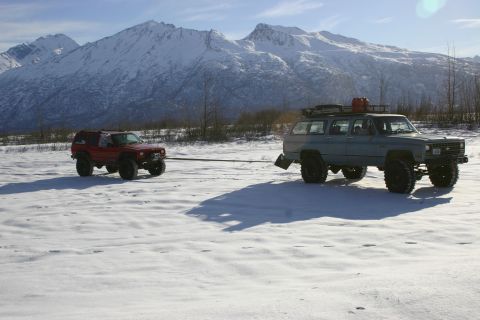 2003 Jeep TJ - Two modified SUVs are parked in a snowy field with mountains in the background.