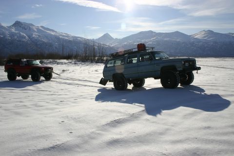 2003 Jeep TJ - Two modified SUVs are seen in a snowy landscape, with one vehicle towing the other.