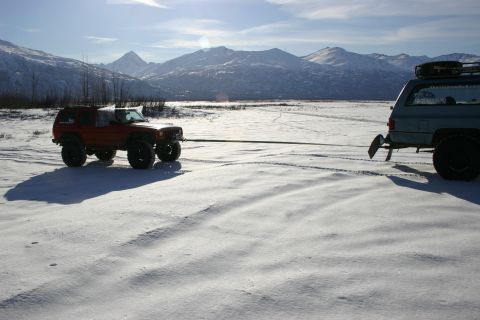 2003 Jeep TJ - Two SUVs are connected by a tow rope in a snowy, mountainous area under a bright sky.