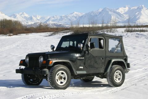 2003 Jeep TJ - A black 2003 Jeep Wrangler navigates a snowy terrain with a mountain range in the background.