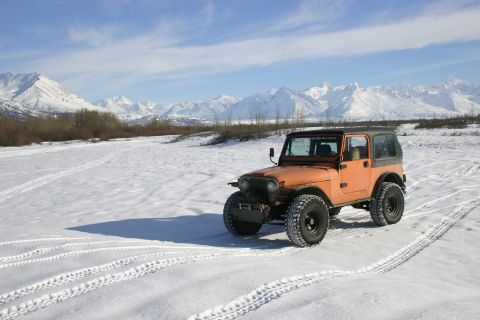 2003 Jeep TJ - An orange Jeep CJ drives through a snowy field with snow-covered mountains in the background.