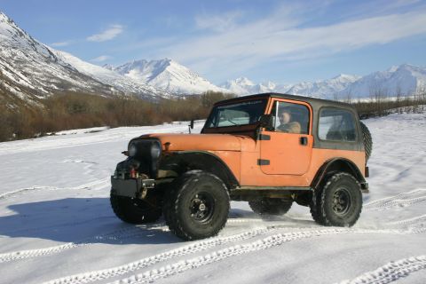 2003 Jeep TJ - Orange Jeep TJ navigates a snowy landscape with snow-covered mountains in the distance.