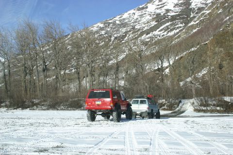 2003 Jeep TJ - Two off-road vehicles, a red Jeep Cherokee and a white SUV, navigate a snow-covered area with a mountain in the background.