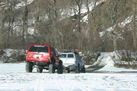 2003 Jeep TJ - Two modified SUVs navigate a snowy trail with a steep incline ahead.
