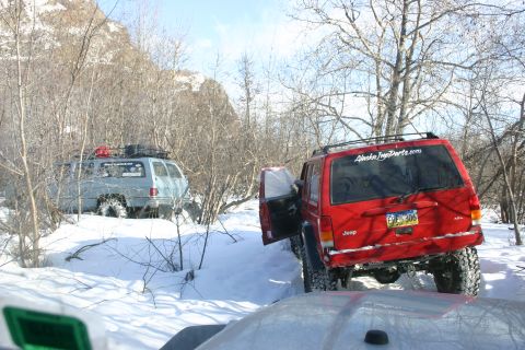 2003 Jeep TJ - Two off-road vehicles are parked in a snowy, wooded area. The red Jeep has its driver's door open.