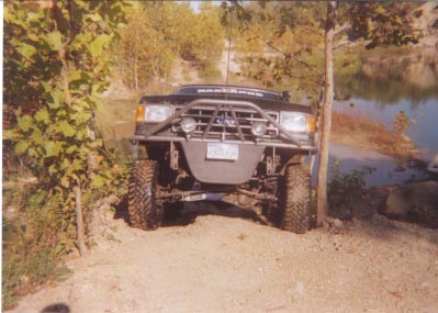 1992 Ford Bronco - Modified 1992 Ford Bronco positioned on a dirt path next to a body of water.