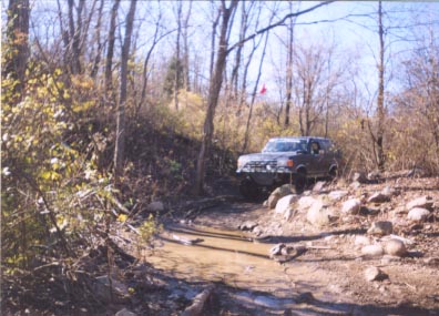 1992 Ford Bronco - A Ford Bronco tackles a challenging off-road course with mud and rocks.