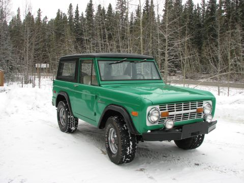 1975 Ford Bronco - A green 1975 Ford Bronco sits in a snowy landscape, its front grille and lights clearly visible.