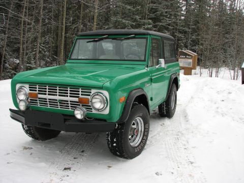 1975 Ford Bronco - A green 1975 Ford Bronco is parked on a snowy path next to a trail marker.