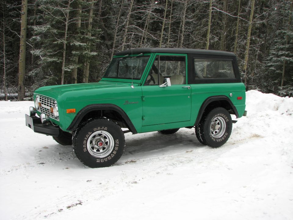 Green 1975 Ford Bronco parked in a snowy area with trees in the background