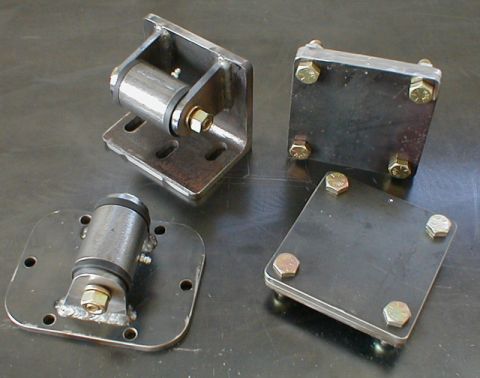 1996 Ford Bronco - Four custom metal brackets, two with rubber dampers and two flat plates, are arranged on a metallic surface.