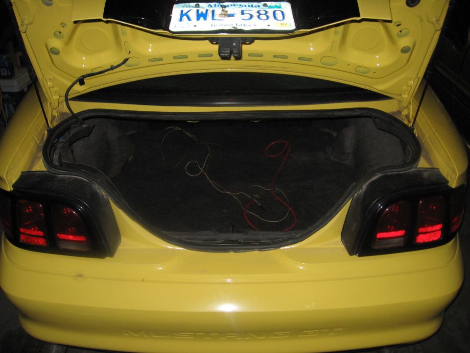 Yellow Ford Mustang rear with open trunk, showing wiring and a Minnesota license plate KWL 580