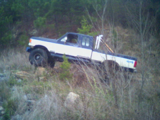 Blue and white extended-cab 4x4 pickup climbing a steep brushy hill, driver-side view