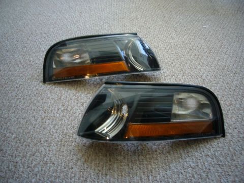 2000 Ford Crown Victoria - Two aftermarket headlights with smoked lenses and amber reflectors are shown on a carpeted surface.
