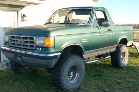 1987 Ford Bronco - This lifted 1987 Ford Bronco is parked on a grassy lawn next to a house.