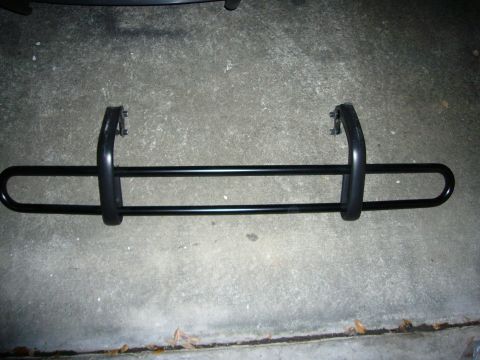 2000 Ford Crown Victoria - A black tubular steel bumper guard/push bar lies on a concrete driveway, showing dual horizontal bars, curved end loops, and two mounting b…