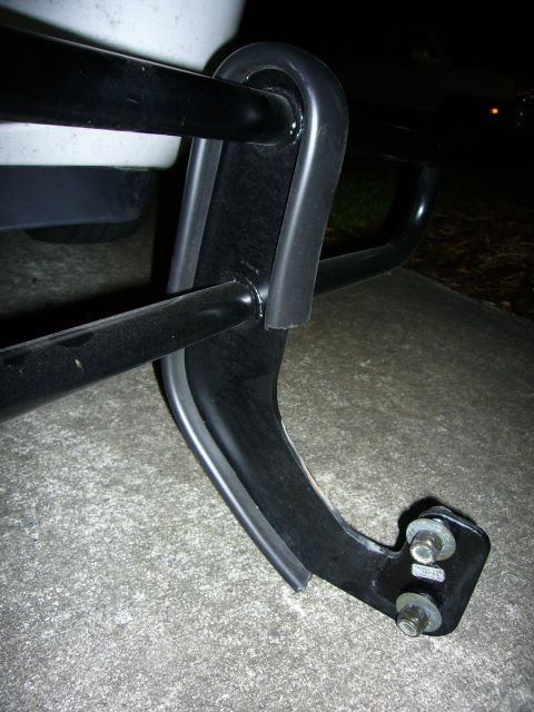 2000 Ford Crown Victoria - Close-up night shot of a black tubular steel push bar or grille guard mounting bracket, bolted to a base plate with hex nuts, resting on a…