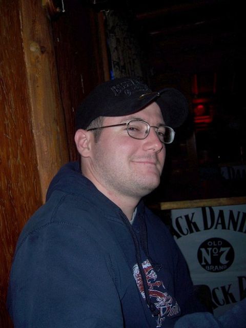 1990 Ford Bronco - Man wearing glasses and a baseball cap, with a Jack Daniel's sign visible behind him.