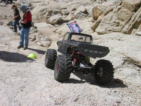 1985 Ford Bronco - A remote-controlled monster truck with a Ford pickup body is shown off-road with large tires and suspension components visible.