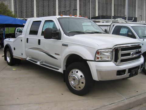 2000 Ford Crown Victoria - A white crew cab tow truck is parked outside a building with another truck beside it.