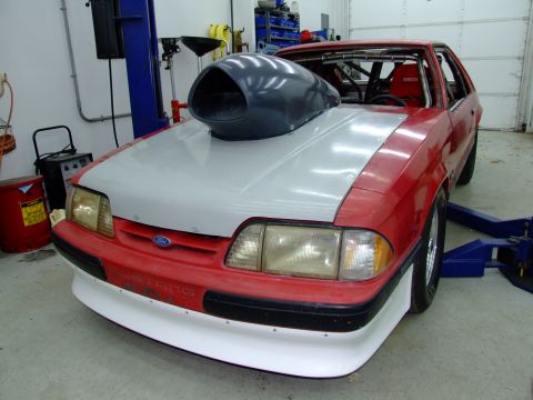 1990 Ford Mustang - A modified 1990 Ford Mustang with a prominent hood scoop sits in a garage, ready for engine work.