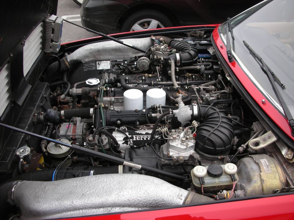 Open engine bay of a red Ferrari showing the engine with Ferrari script