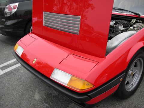 1998 Ford Crown Victoria - The front of a red Ferrari is shown with its hood open, revealing the engine compartment. A black vehicle is visible behind it.