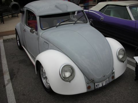 1998 Ford Crown Victoria - A customized Volkswagen Beetle, painted gray and white, with a unique exhaust pipe, parked next to a purple convertible.