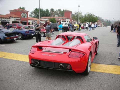1998 Ford Crown Victoria - A red Porsche Carrera GT is parked at a car meet, with other vehicles and people in the background.