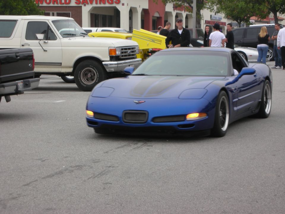 Front of a blue Chevrolet Corvette C5 with headlights on at a car show