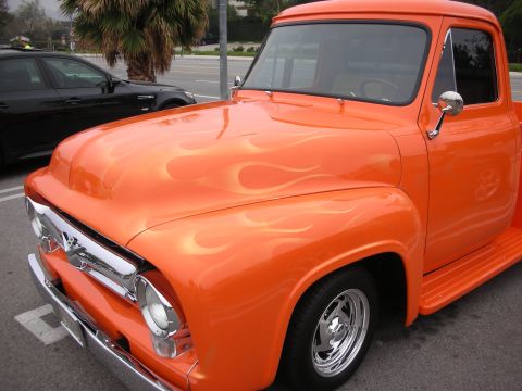 1998 Ford Crown Victoria - An orange pickup truck with flame decals is parked next to a black car.