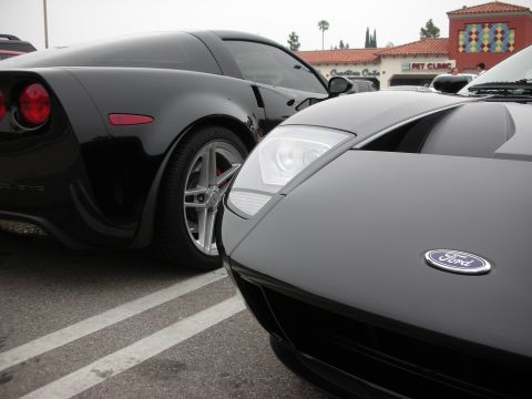 1998 Ford Crown Victoria - A black Ford GT is parked next to a black Chevrolet Corvette, with a "Creative Cafe" and "Pet Clinic" visible in the background.