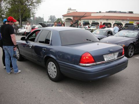 1998 Ford Crown Victoria - A blue sedan is parked in a lot with other vehicles and people milling around.
