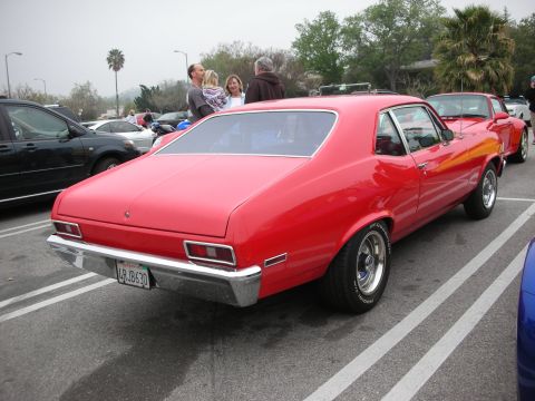 1998 Ford Crown Victoria - A bright red classic coupe is parked in a lot, with other vehicles and people in the background.