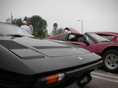 1998 Ford Crown Victoria - A black sports car is parked next to a red sports car, with people gathered in the background.
