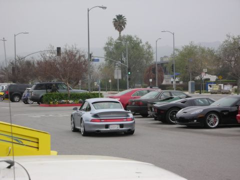 1998 Ford Crown Victoria - A silver Porsche 911 is parked in a lot with other vehicles, including a black Chevrolet Corvette and a red sedan.